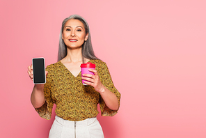 smiling woman with coffee to go showing smartphone with blank screen on pink