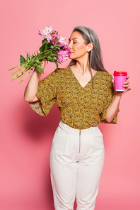 mature woman with takeaway drink enjoying flavor of peonies on pink background