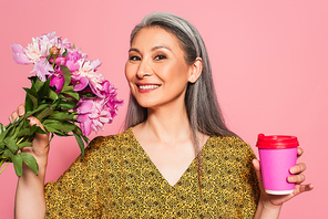 cheerful woman with flowers and coffee to go  isolated on pink