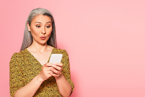 surprised woman in patterned blouse messaging on cellphone isolated on pink