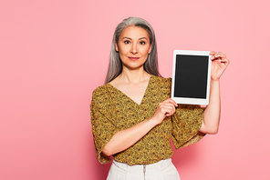 mature woman showing digital tablet with blank screen on pink background