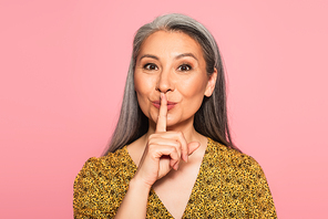 positive grey haired woman showing hush sign while  isolated on pink