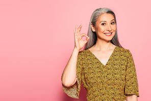 happy mature woman in yellow blouse with pattern showing okay gesture on pink background