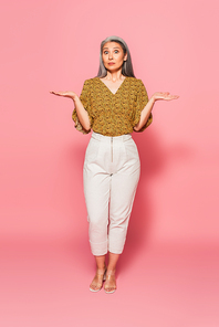 full length view of shocked mature woman pointing with hands on pink background