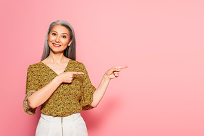 mature, positive woman pointing with fingers while smiling at camera on pink background