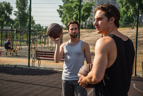 Man holding basketball ball near blurred friend on playground