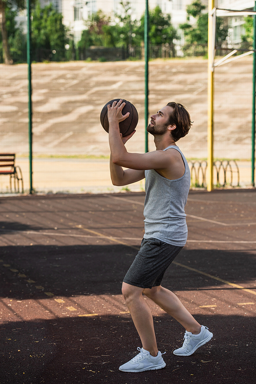 Side view of young man holding basketball ball on outdoor playground