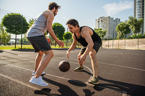Side view of men in sportswear playing basketball on court outdoors
