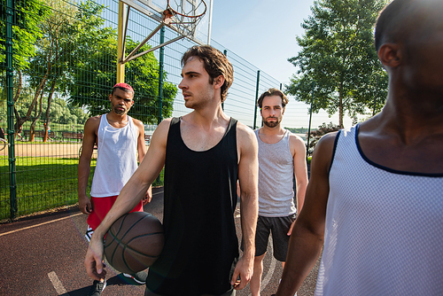 Young man holding basketball ball near multiethnic friends outdoors