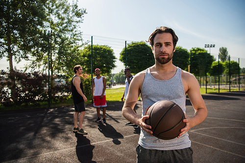 Man with basketball ball  near interracial friends on court