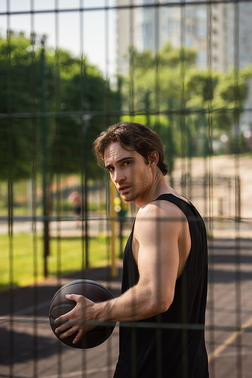 Young man with basketball ball  near fence outdoors