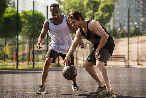 Smiling interracial men playing basketball outdoors