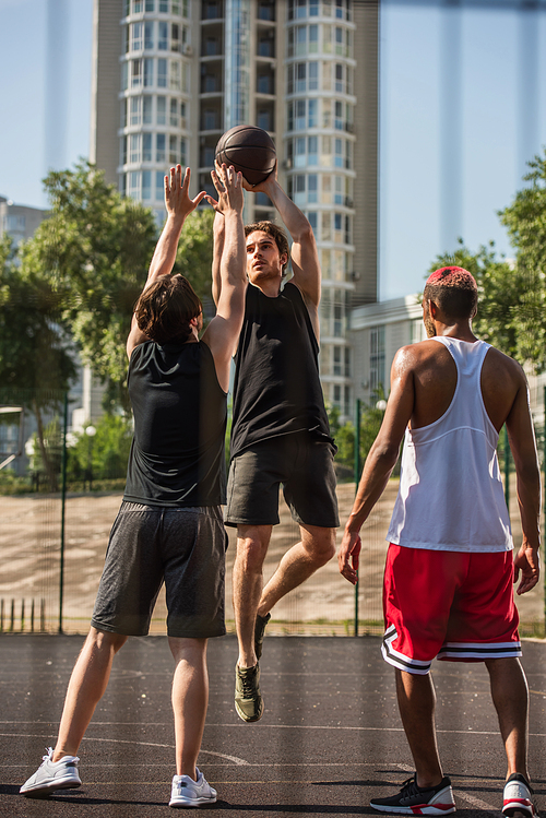 Sportsman with basketball ball jumping near interracial sportsmen outdoors