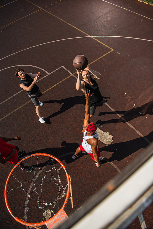 Overhead view of man with basketball ball jumping near interracial friends and hoop outdoors