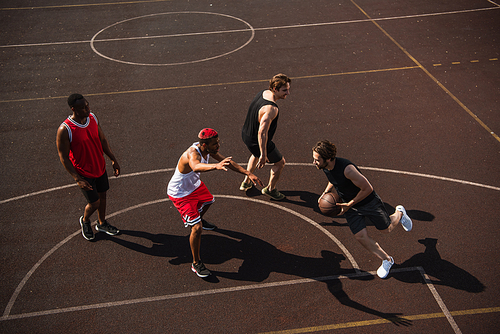 High angle view of man with basketball ball running on playground near multiethnic friends