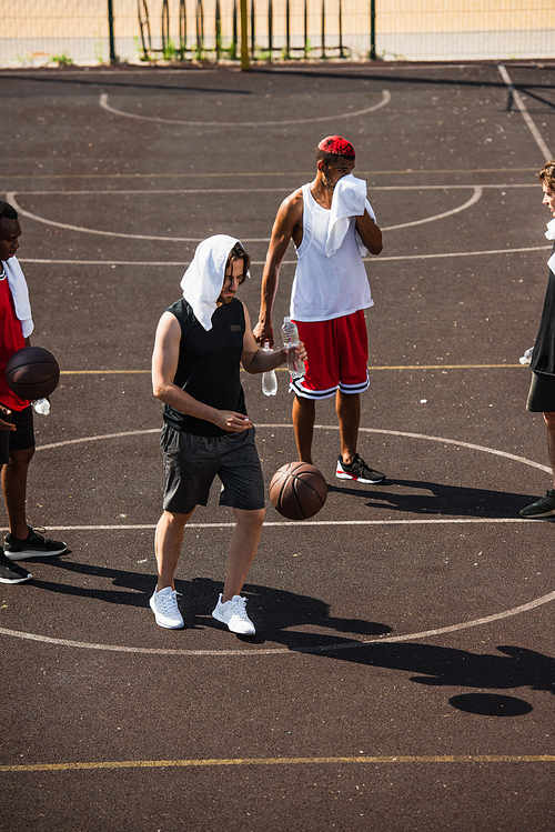 Young man with towel and water standing near basketball ball and multiethnic friends