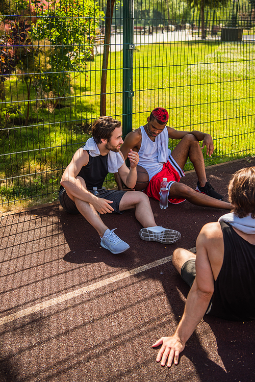 Young sportsman with towel talking to interracial friends on basketball playground