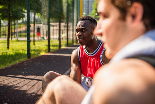 Smiling african american sportsman sitting near blurred friend on foreground