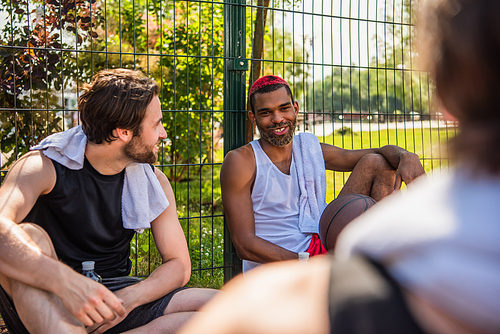 Smiling african american sportsman with basketball ball talking at friends outdoors