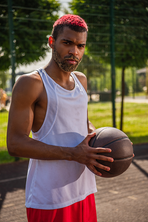 African american sportsman with dyed hair holding basketball ball and  outdoors