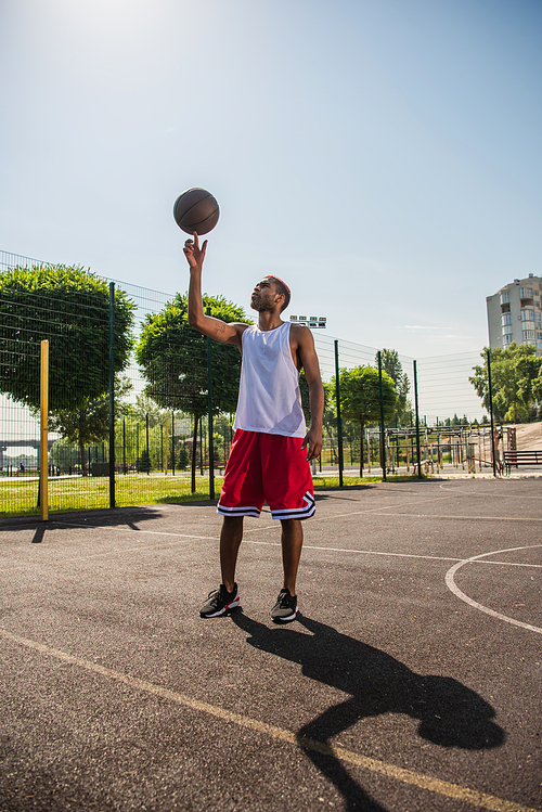 Side view of african american sportsman holding basketball ball on finger on playground