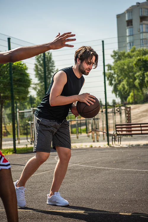 Side view of man playing basketball near blurred african american friend
