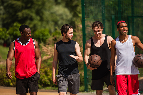 Interracial sportsmen with basketball balls walking outdoors