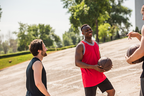 Cheerful african american basketball player with ball looking at friends outdoors