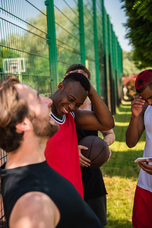 Interracial basketball players with ball and smartphone laughing outdoors