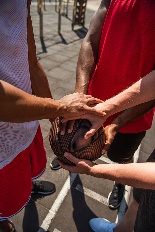 Cropped view of interracial sportsmen holding hands on basketball ball
