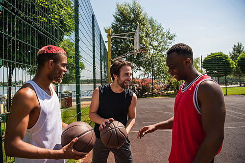 Smiling man holding basketball near african american friends on playground