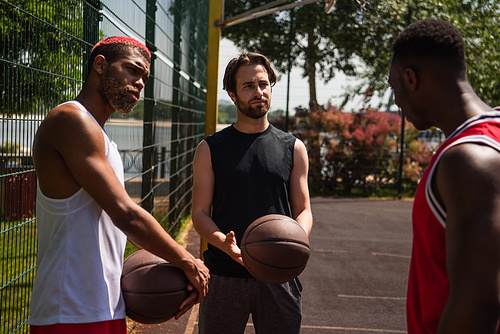 Young sportsmen with basketball balls looking at african american friend on playground