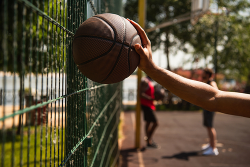 Cropped view of african american sportsman holding basketball ball near fence outdoors