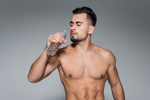 muscular sportsman holding bottle with water isolated on grey