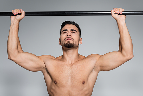 muscular young sportsman exercising on horizontal bar isolated on grey