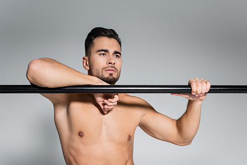 muscular sportsman looking away and leaning on horizontal bar isolated on grey