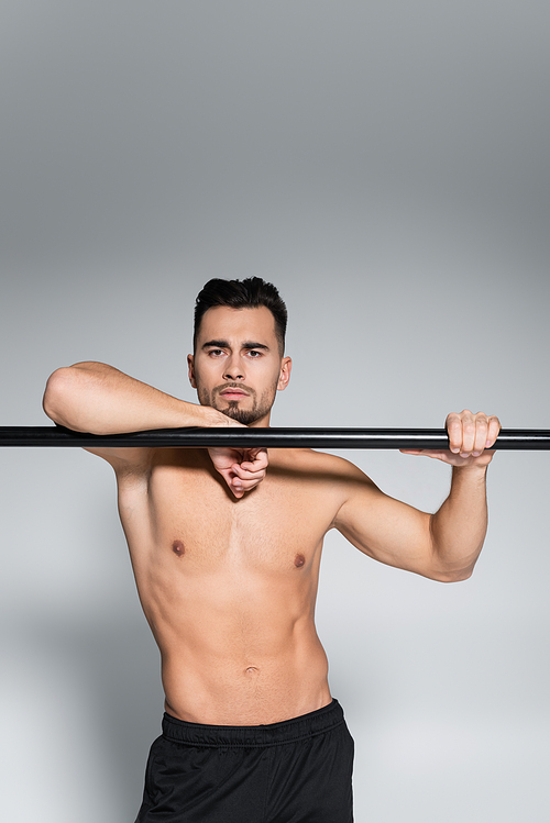 muscular sportsman  and leaning on horizontal bar on grey