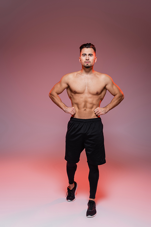 full length of lighting on shirtless man with muscles posing on pink and grey