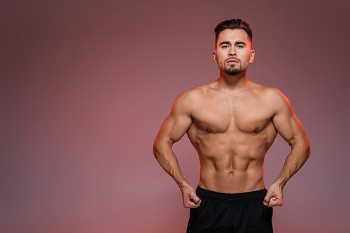 red lighting on strong man with muscles posing on pink and grey