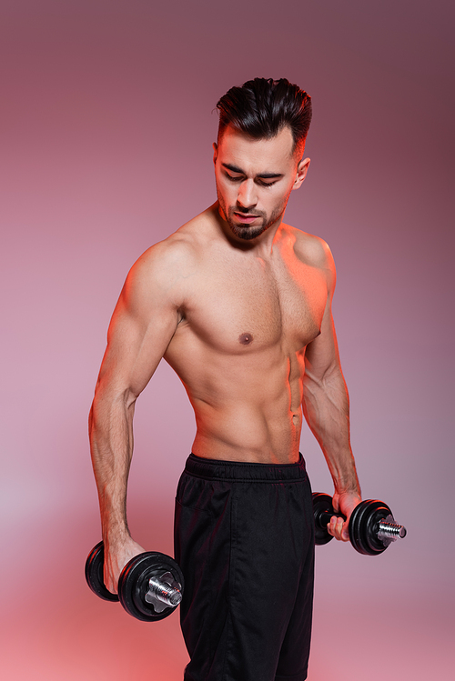 strong sportsman working out with dumbbells on pink and grey