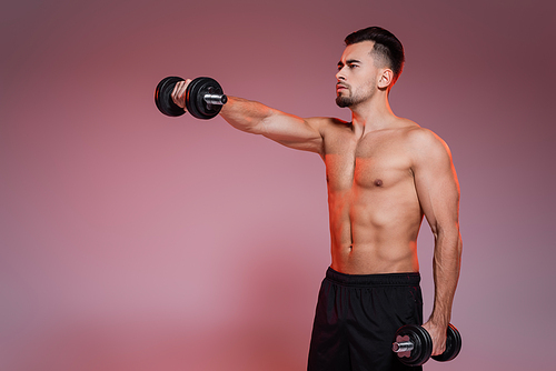 shirtless man training with dumbbells and looking away on pink and grey