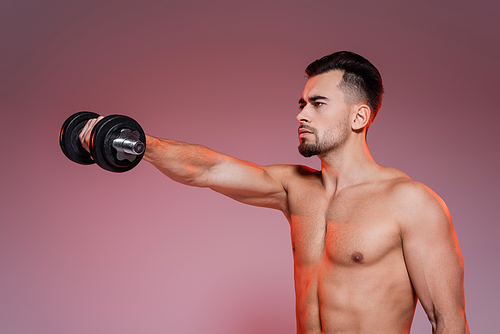 strong and shirtless man training with dumbbell and looking away on pink and grey