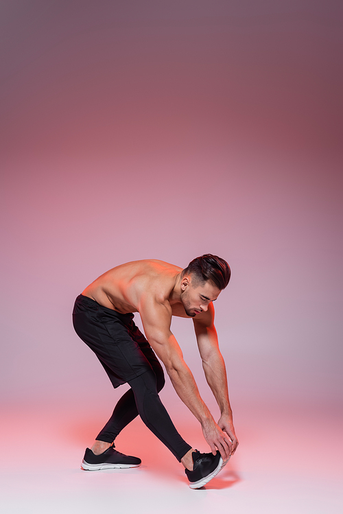 shirtless sportsman leaning while stretching on grey and pink