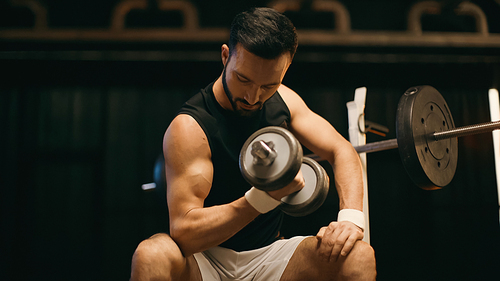 Brunette sportsman working out with dumbbell on dark background