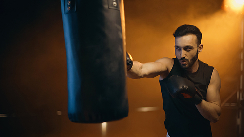 Sportsman training with punch bag on dark background