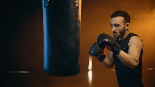 Athletic boxer training with punch bag on dark background