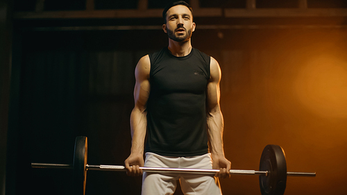 Athletic sportsman holding barbell on dark background