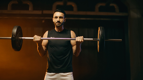 Brunette sportsman training with barbell on dark background