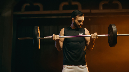 Athletic man training with barbell on dark background