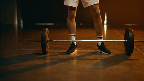 Cropped view of sportsman standing near barbell on dark background